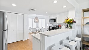 Una cocina moderna con armarios blancos, una isla central con taburetes, un microondas y una lámpara colgante.