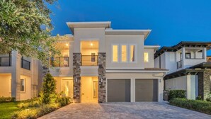 A modern two-story house with a stone facade, a covered garage, and a well-maintained lawn. - Stunning and luxe Bears Den Luxury Villa w/ Outdoor Kitchen near Disney (Kissimmee)