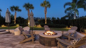 An outdoor patio with a fire pit, lounge chairs, and umbrellas. - Stunning and luxe Bears Den Luxury Villa w/ Outdoor Kitchen near Disney (Kissimmee)