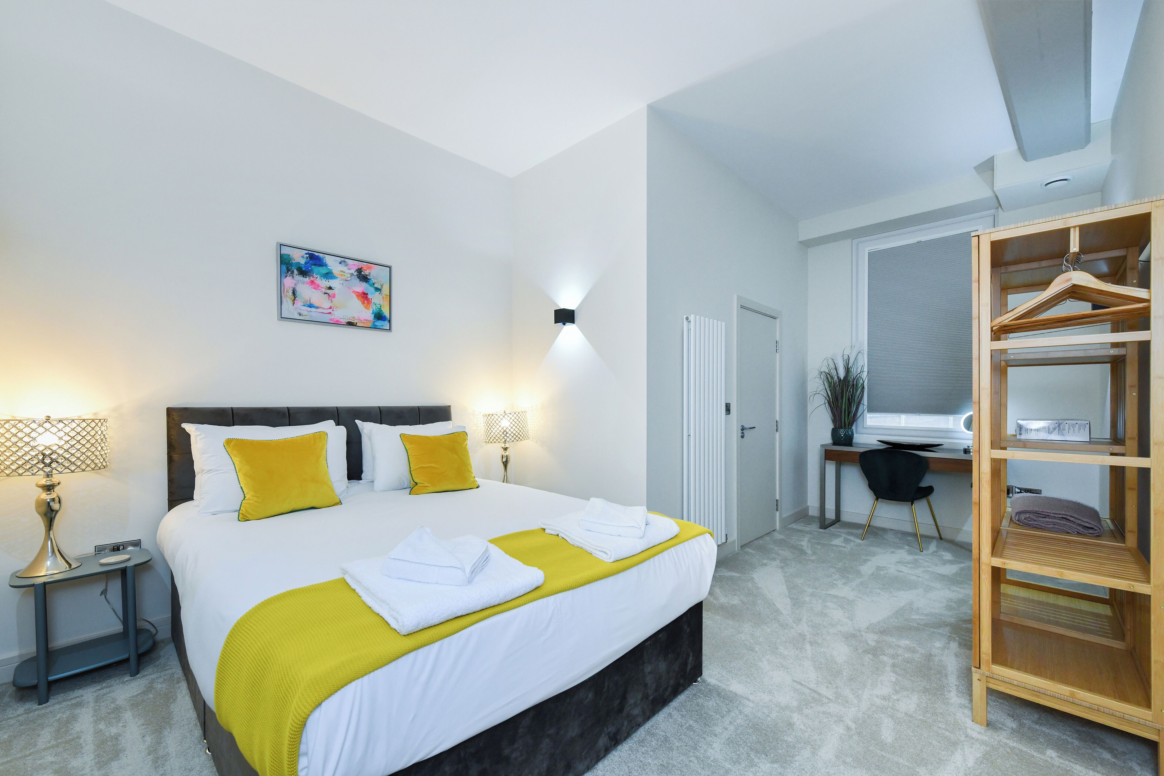 Una habitación de hotel moderna con una cama grande, lámparas de noche, un escritorio y un armario.