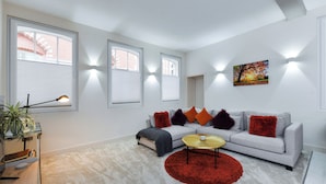 Un salon moderne avec un canapé gris, des coussins rouges et orange, un tapis rouge et un tableau accroché au mur.