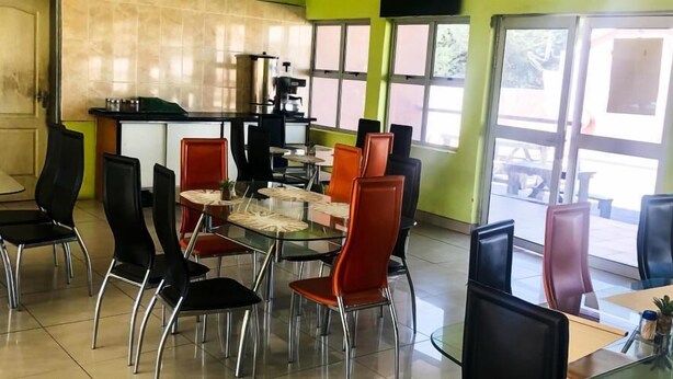 Un restaurante con zona de comedor de cristal, sillas negras y rojas, y una máquina de café.