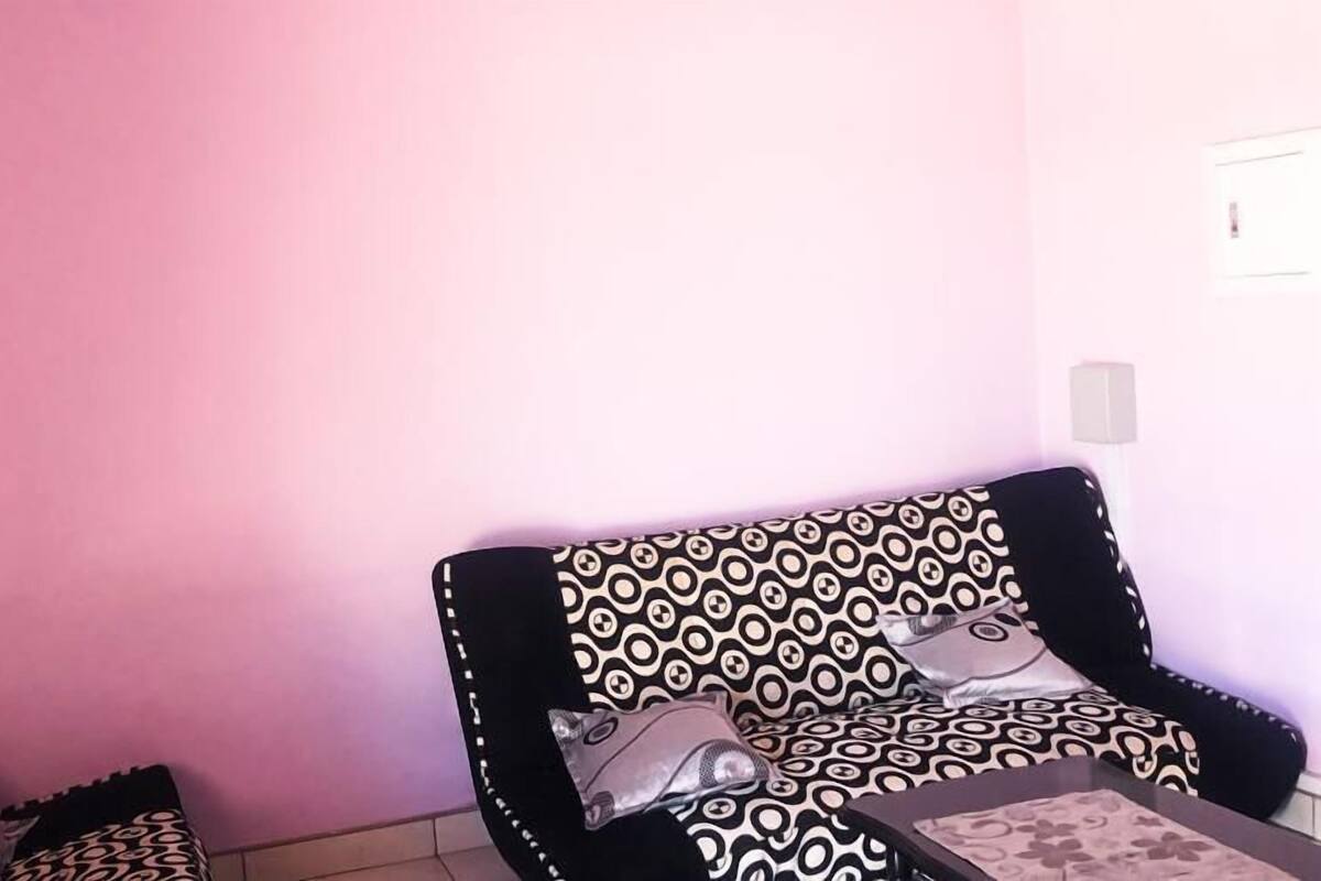 A room with a pink wall, a patterned armchair, and a small table with a cushion.