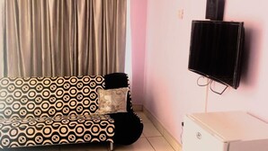 Una sala de estar con un sofá estampado, un televisor montado en la pared y un mueble blanco pequeño.