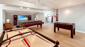 Una sala de estar con mesa de billar, mesa de fútbolín y televisor mostrando una playa.