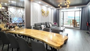 A modern dining area with a long wooden table, grey upholstered chairs, and a sofa with cushions. - 3-bedroom Oasky Vung Tau with Partial Ocean View (Vung Tau)