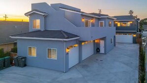 Une maison moderne à deux étages, dotée d’un toit plat, de plusieurs portes de garage et d’une allée.