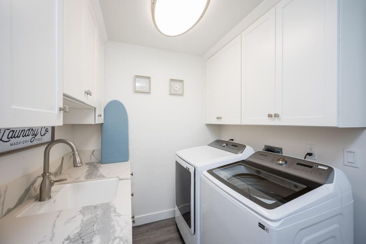 A laundry room with a sink, two washing machines, and a dryer.