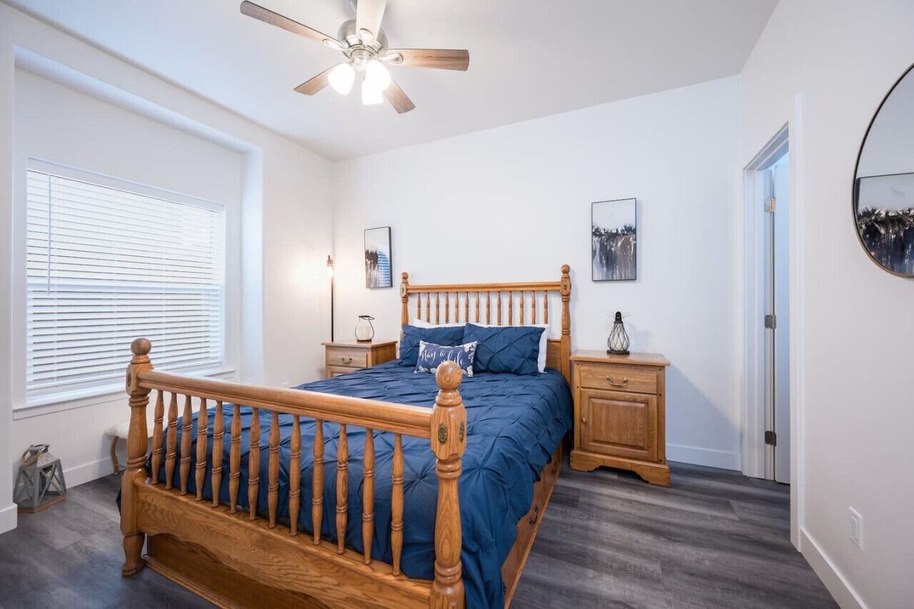 A bedroom with a wooden bed, a ceiling fan, a nightstand, a dresser, and a window with blinds.