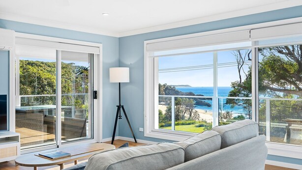 A modern living room with a sofa, a floor lamp, and large windows offering a view of the sea and greenery. - 198 Mystery Bay Road, Mystery Bay (Mystery Bay)