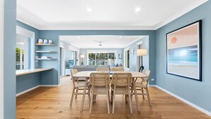 A spacious dining area with a wooden table and wicker chairs, leading to a kitchen and a living area with a large window. - 198 Mystery Bay Road, Mystery Bay (Mystery Bay)
