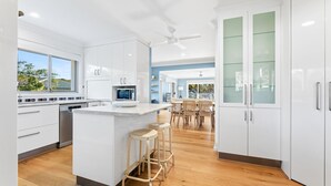A modern kitchen with white cabinetry, a central island, and a dining area with wooden chairs. - 198 Mystery Bay Road, Mystery Bay (Mystery Bay)