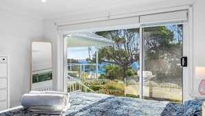 A bedroom with a bed, a nightstand, a dresser, and a large sliding glass door leading to a balcony with a view of the sea and a tree. - 198 Mystery Bay Road, Mystery Bay (Mystery Bay)