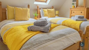 Une chambre avec deux lits, une literie jaune, un puits de lumière, une commode en bois et une petite plante.