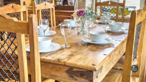 Une table de salle à manger en bois, dressée avec de la vaisselle blanche et des verres, entourée de chaises en bois.