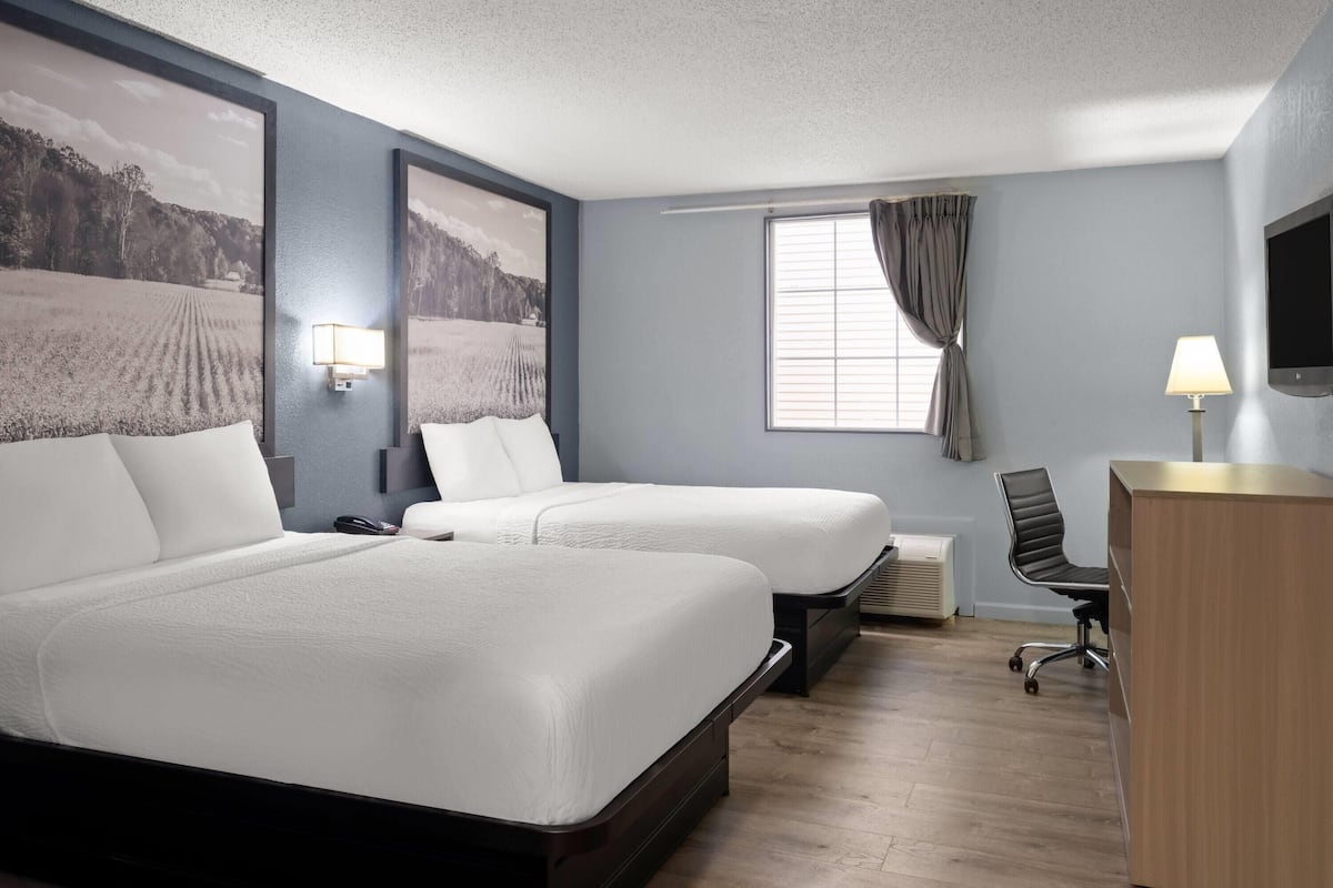 A hotel room with two beds, a desk, a chair, a television, and a window with curtains.