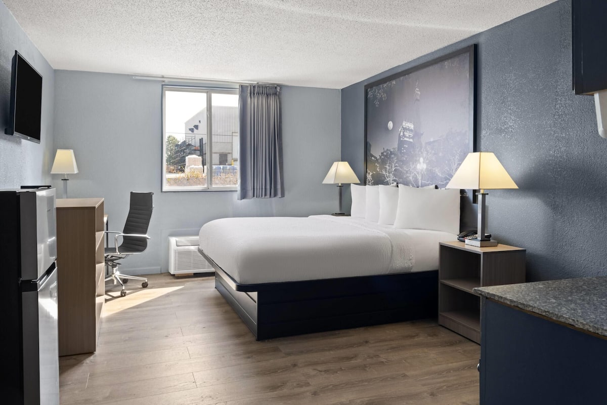 A modern hotel room with a bed, desk, chair, and a large window with curtains.