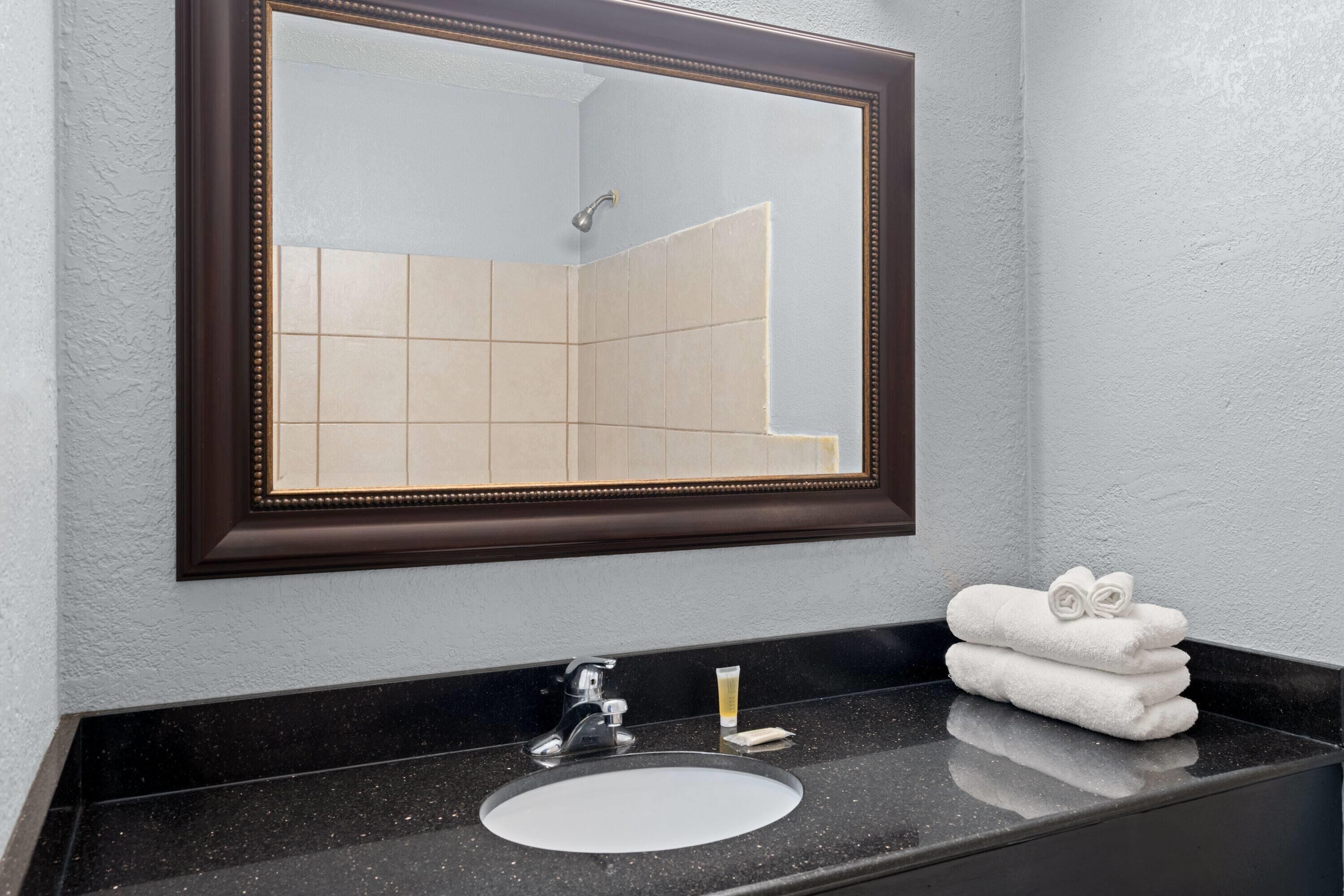 A bathroom with a large mirror, a sink, and a towel rack.