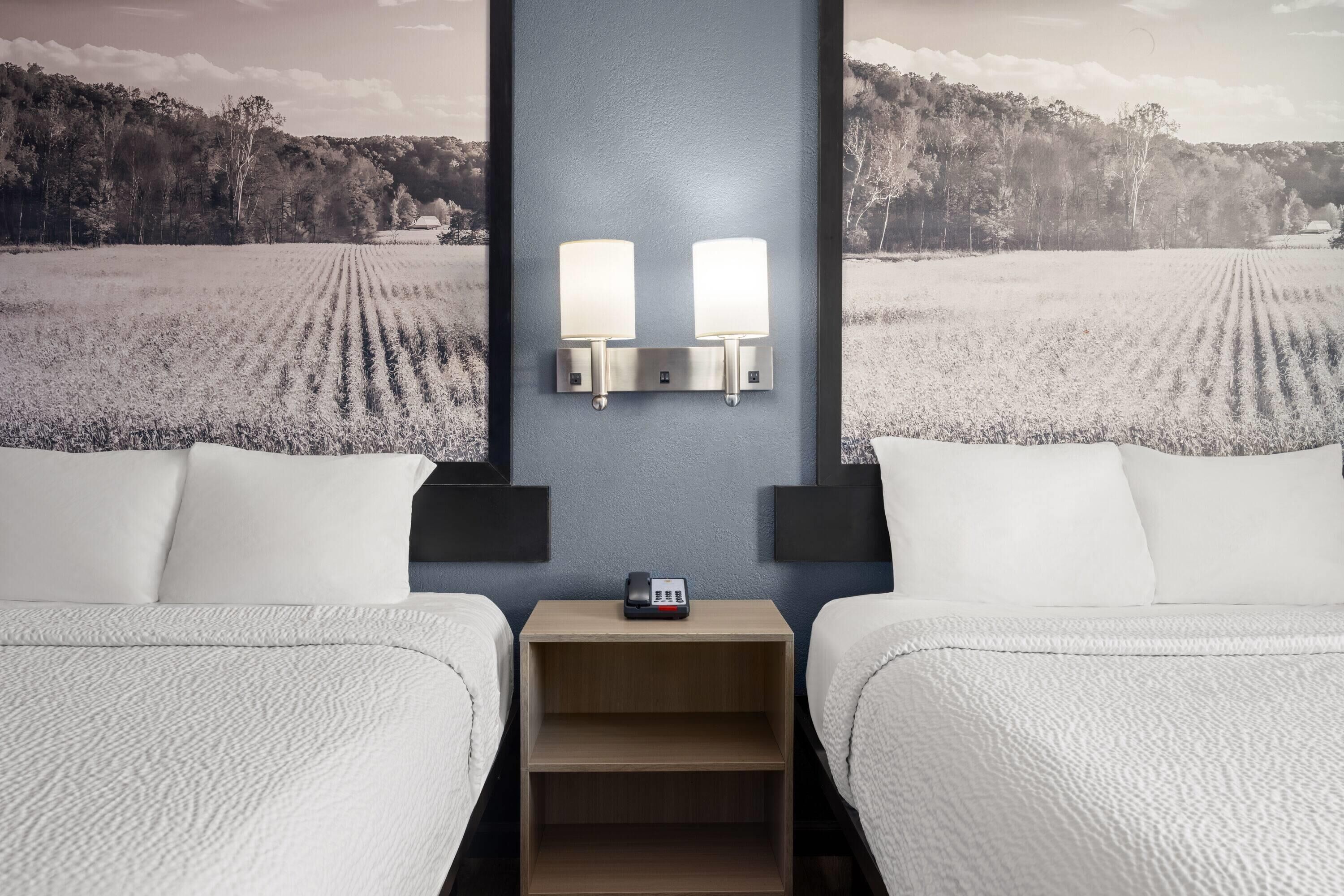 A hotel room with two beds, a nightstand with a phone, and wall-mounted lights.