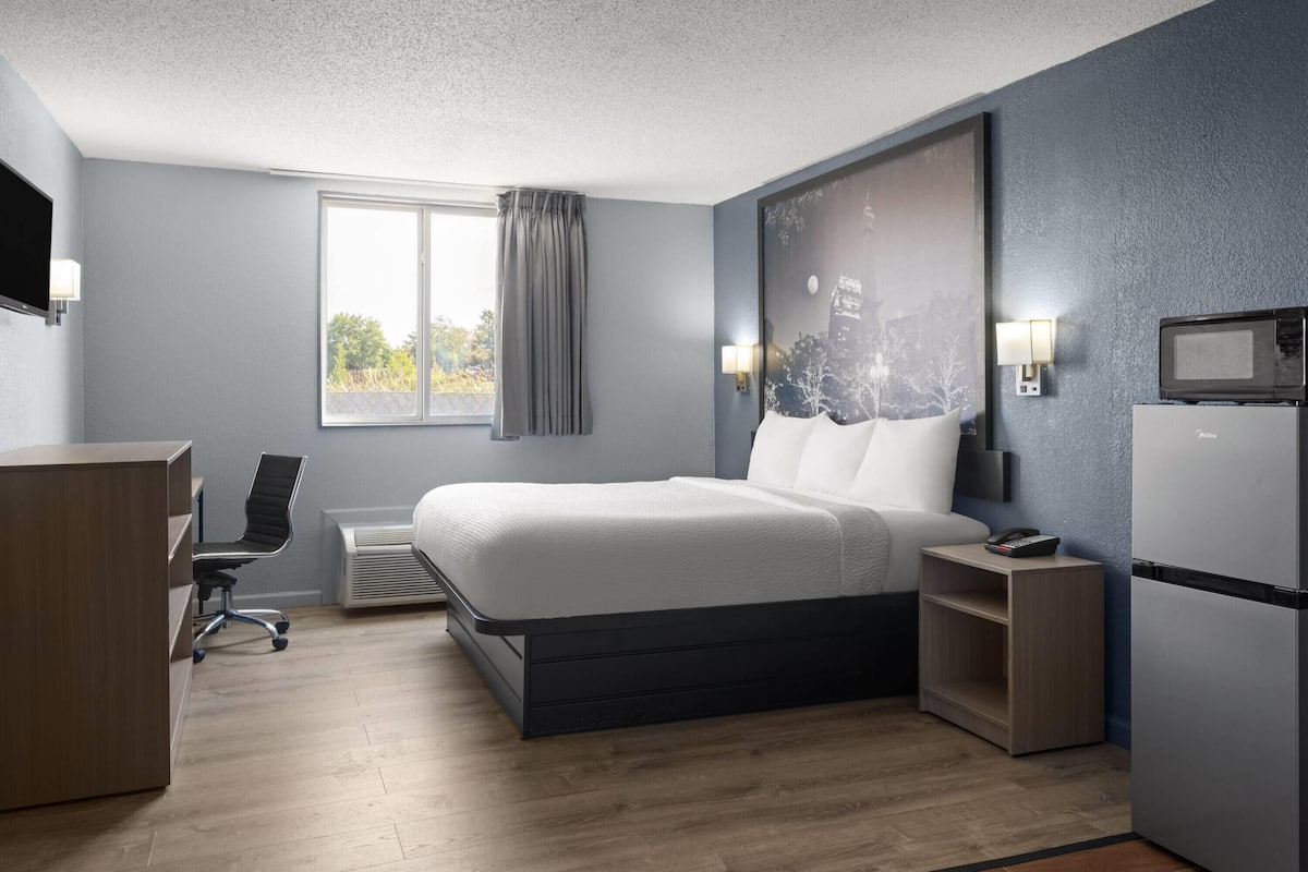 A modern hotel room with a bed, desk, chair, and a flat-screen TV.