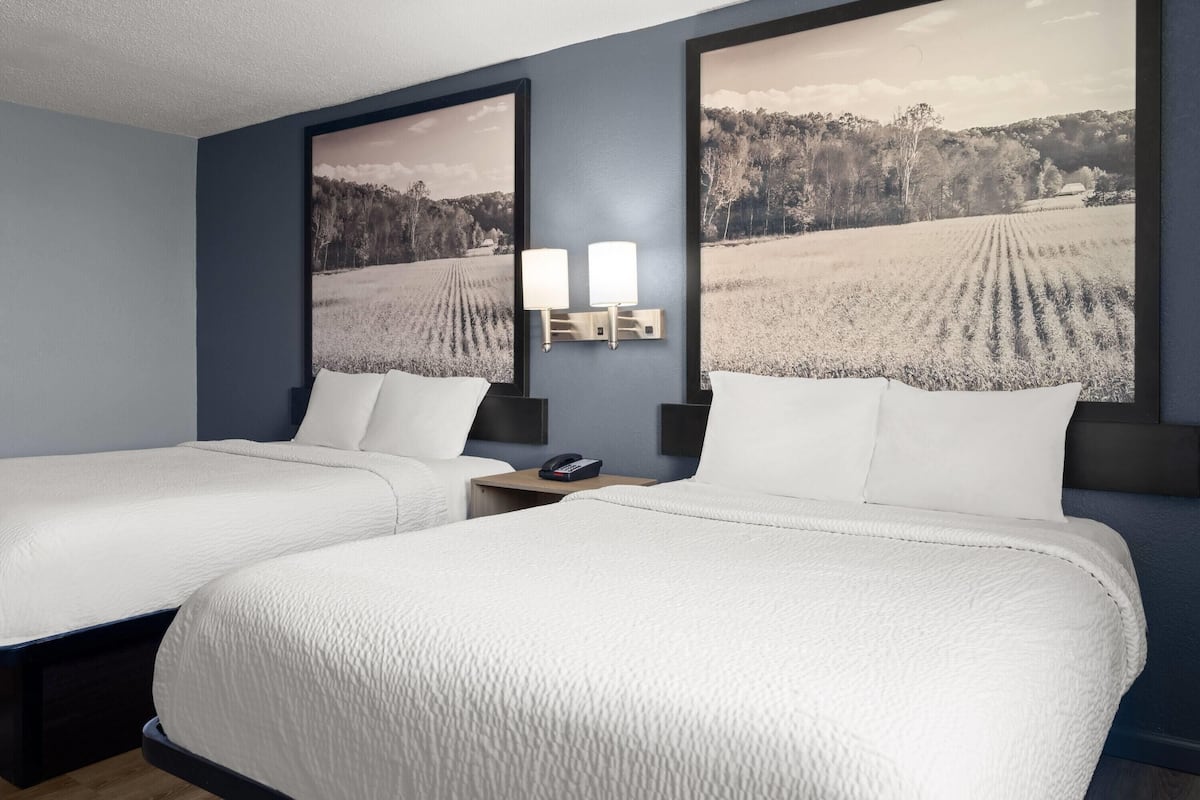 A hotel room with two beds, a nightstand, a telephone, and two wall-mounted lamps.
