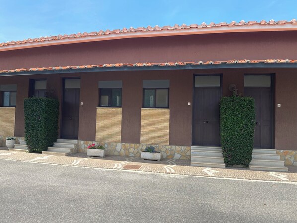 A modern building with a flat roof, multiple doors, and a stone base. - American Motel (Cisterna di Latina)