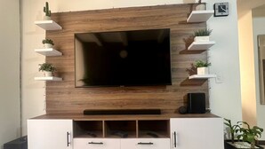 A modern living room with a large flat-screen TV mounted on a wooden wall, surrounded by white cabinets and shelves with plants. - Acogedor Apto en Bello, cerca del Metro y Centro Comercial (Bello)