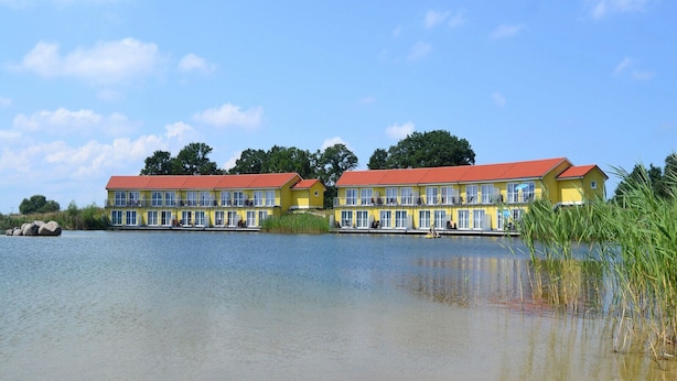 Ein gelbes Gebäude mit rotem Dach am Seeufer, ausgestattet mit zahlreichen Fenstern und Balkonen.