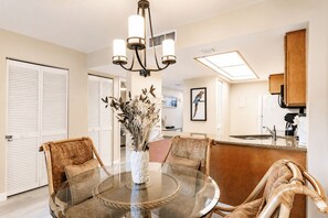 A dining area with a round glass table, wicker chairs, a chandelier, and a vase with dried flowers. - Park Shore Resort, BLDG G #241*Great Views* (Park Shore Resort)