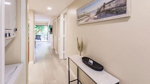 Ein Flur mit weißer Wand, einem gerahmten Bild, einem kleinen Tisch mit einer Dekoration und einer Tür zu einem anderen Raum.