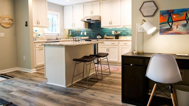 A modern kitchen with white cabinets, a central island, bar stools, and a dining area with a chair.