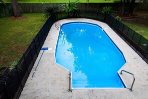 En rektangulär swimmingpool med ett svart säkerhetsstaket, omgiven av en gräsyta och träd.
