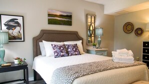 A bedroom with a large bed, a nightstand, a lamp, and wall art.