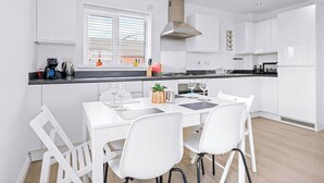 A modern kitchen with white cabinets, a black countertop, and a dining area with white chairs. - Bridge House by Tŷ SA (Newport)