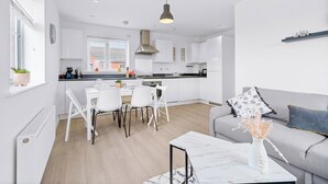 A modern kitchen with white cabinets, a dining area with white chairs, and a grey sofa with a vase of dried flowers. - Bridge House by Tŷ SA (Newport)