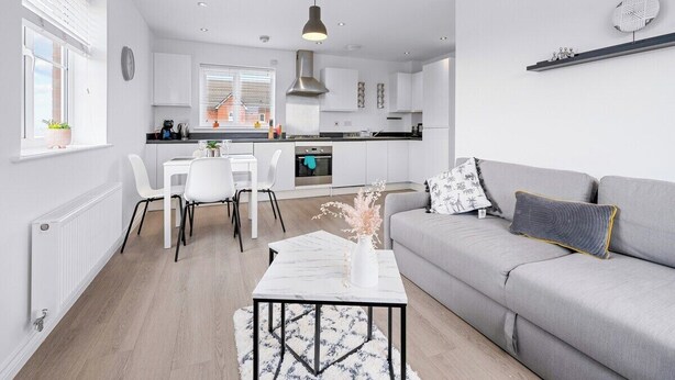 A modern living room with a grey sofa, a coffee table, and a dining area with white chairs and a white table. - Bridge House by Tŷ SA (Newport)