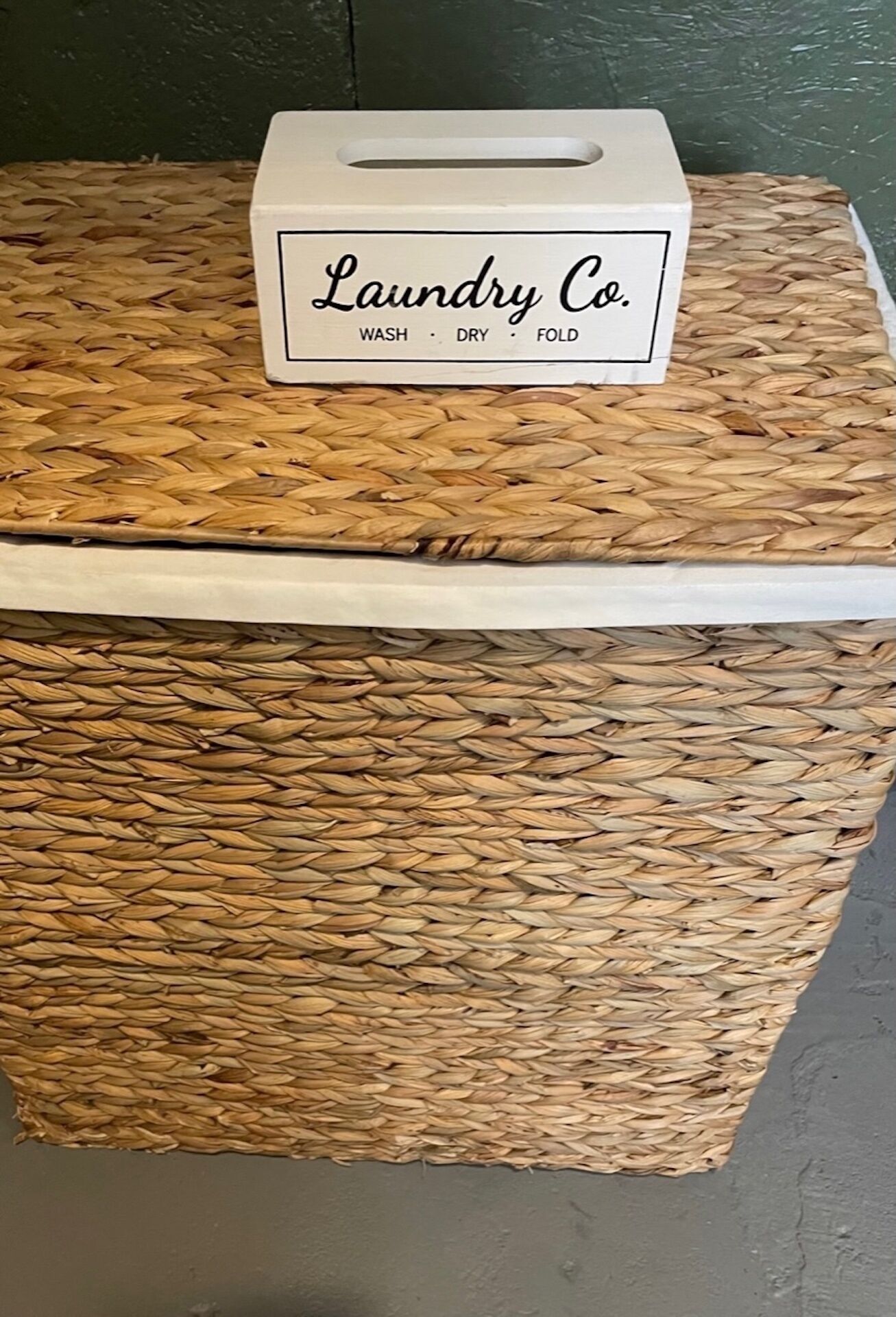 A woven basket with a white label that reads "Laundry Co." and lists services: wash, dry, fold.