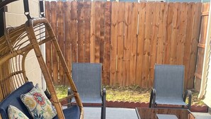 A patio area with a wicker rocking chair, two cushioned chairs, and a glass-top table. - Home in Anderson Township (Cincinnati)