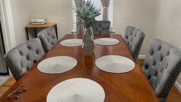 A dining room with a wooden table, grey upholstered chairs, a vase with flowers, and a small side table with books. - Home in Anderson Township (Cincinnati)