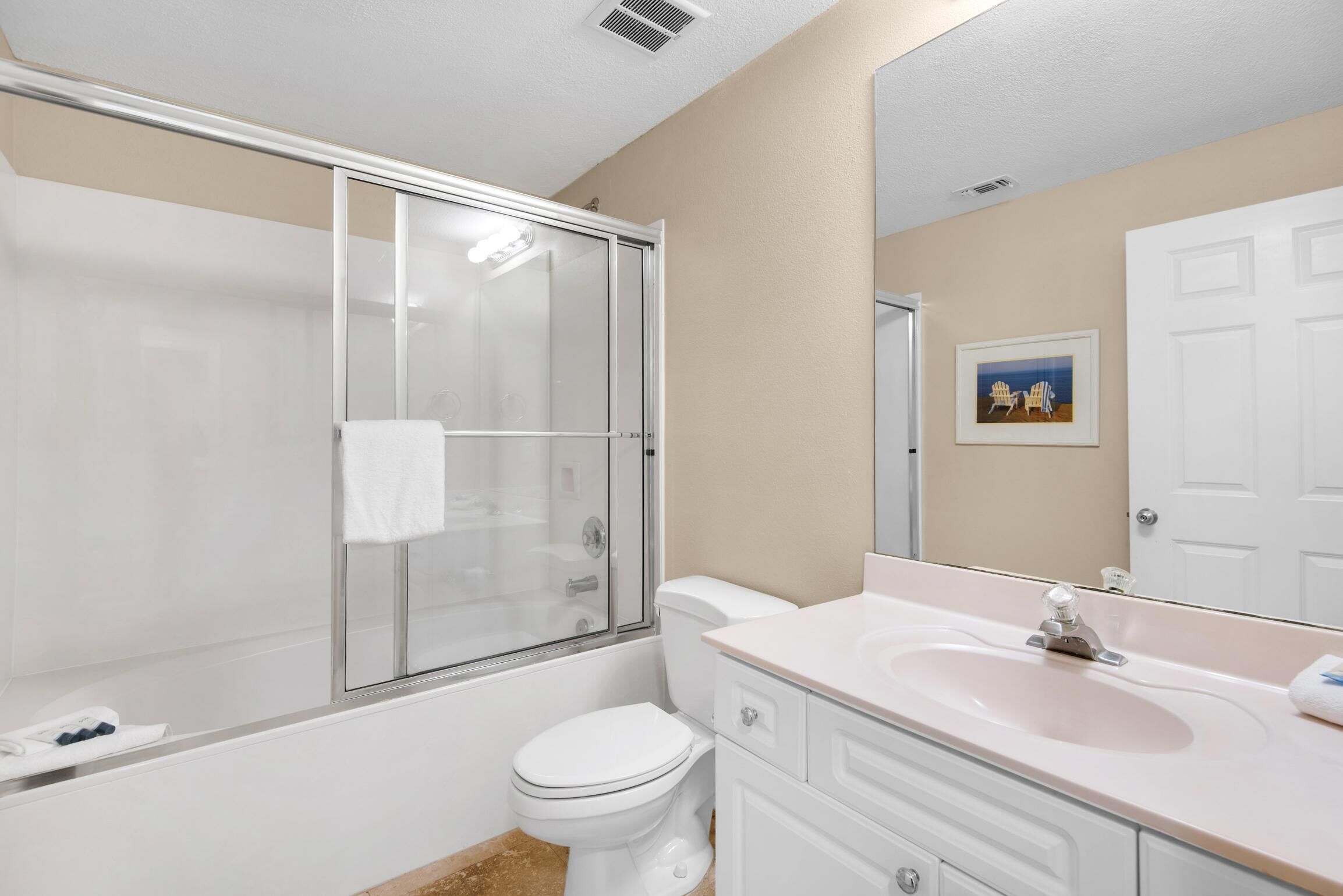 A bathroom with a glass-enclosed shower, a white toilet, a sink with a mirror, and a framed picture on the wall.