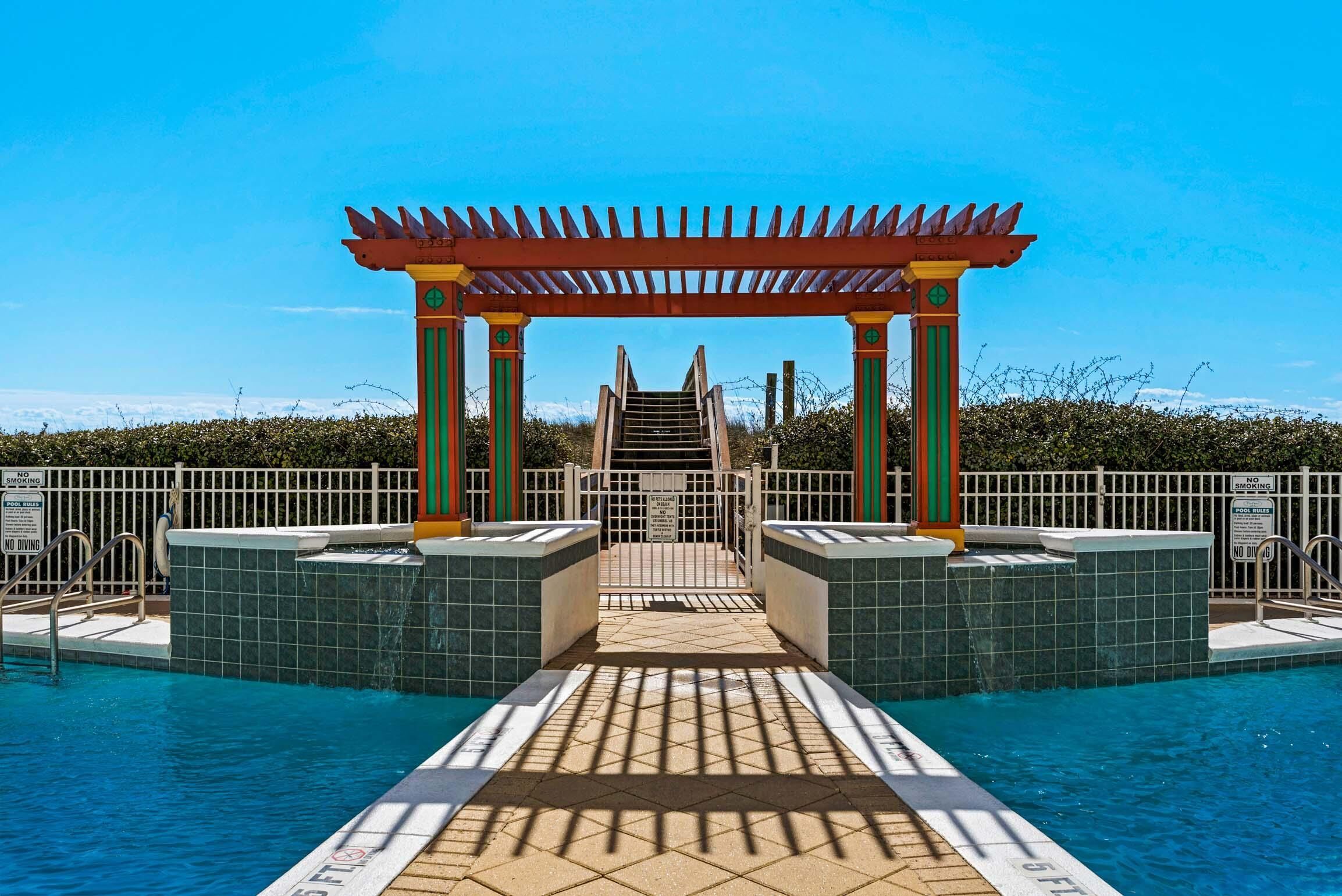 A pool area with a covered walkway leading to the pool, surrounded by a fence and signs indicating pool rules.