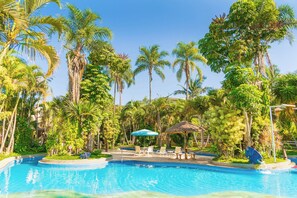 A swimming pool surrounded by palm trees and a thatched-roof structure. - Hotel Mil Flores (Braganca Paulista)