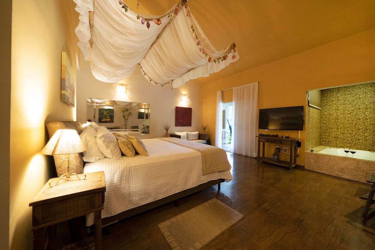 Ein Schlafzimmer mit einem großen Bett, Nachttischlampen, einem Fernseher, einer Badewanne und einem Spiegel.
