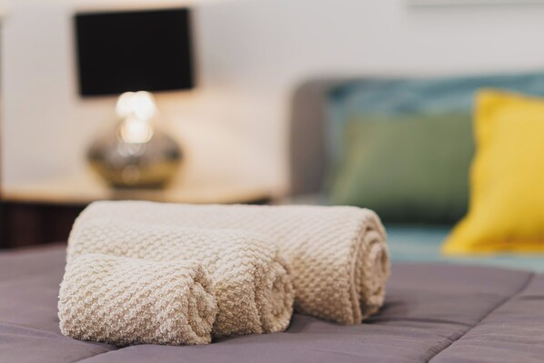 A neatly folded beige blanket on a bed with a dark-colored headboard and a green pillow in the background.