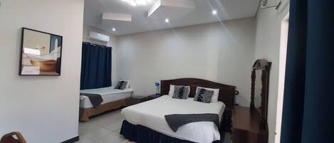 A hotel room with two beds, a ceiling fan, an air conditioning unit, and a wooden headboard.