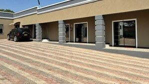 Um edifício com telhado plano, área de entrada pavimentada e um carro estacionado.