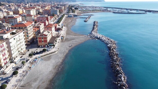 An aerial view of a coastal city with a rocky breakwater, buildings along the shore, and a clear blue sea. - Verdemare  (Chiavari)