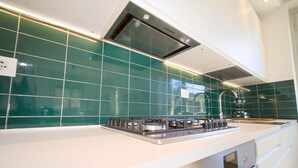 A modern kitchen with a gas stove, stainless steel appliances, and green tiled backsplash. - Verdemare  (Chiavari)