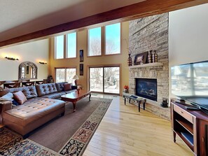 A spacious living room with a large leather sofa, a stone fireplace, and a television. - A Shore Thing by Taylor Made Deep Creek (McHenry)