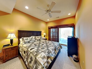 A bedroom with a bed, two bedside lamps, a ceiling fan, a nightstand, a dresser, and a window with curtains. - A Shore Thing by Taylor Made Deep Creek (McHenry)